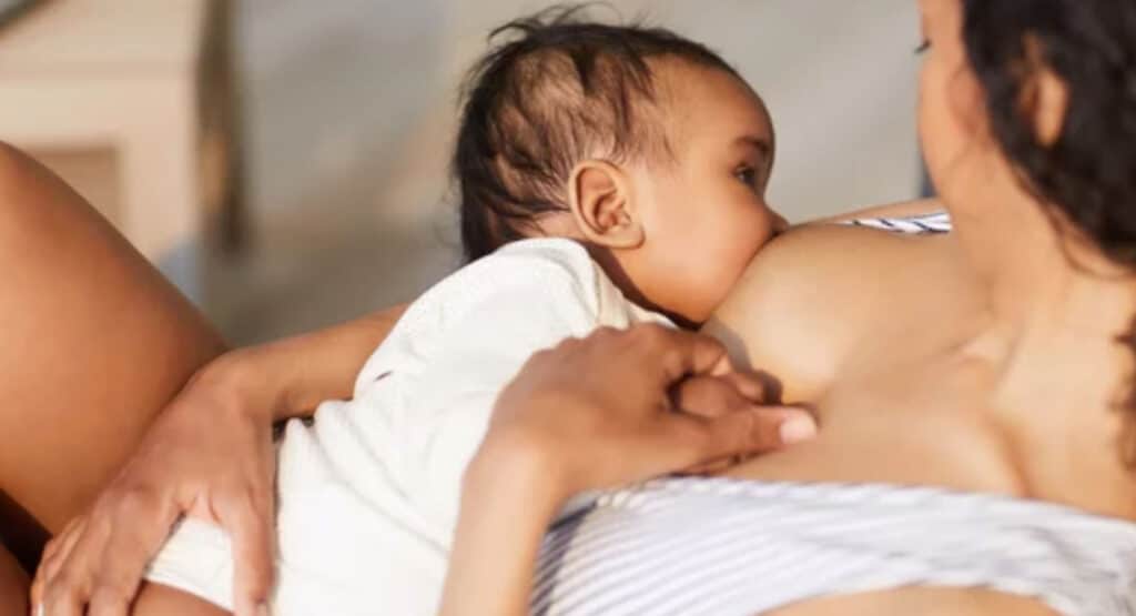 Close-up of young black mother attaching baby at breast while giving nipple to son during breastfeeding
