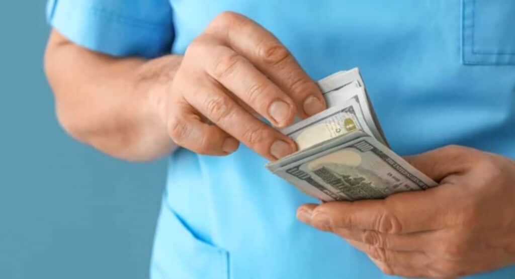 Mature doctor with bribe on blue background, closeup
