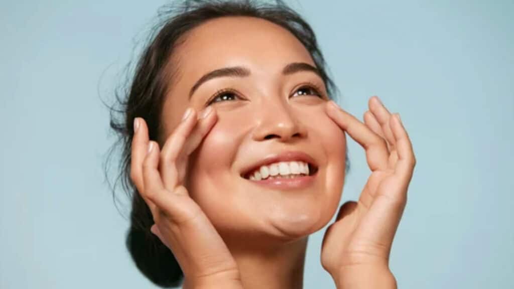 Skin care. Woman with beauty face touching healthy facial skin portrait. Beautiful smiling asian girl model with natural makeup touching glowing hydrated skin