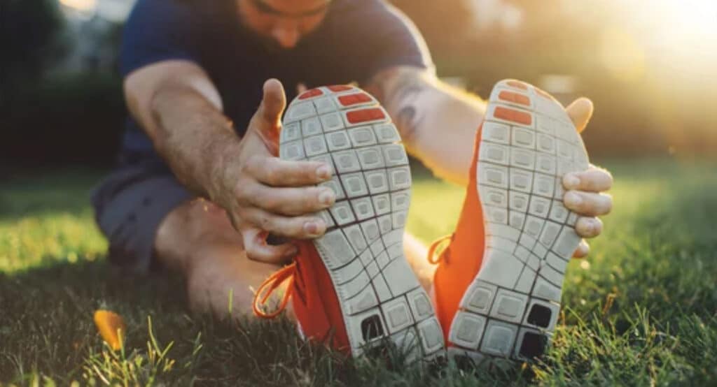 Attractive young man stretching in the park before running at the sunset focus on shoes
